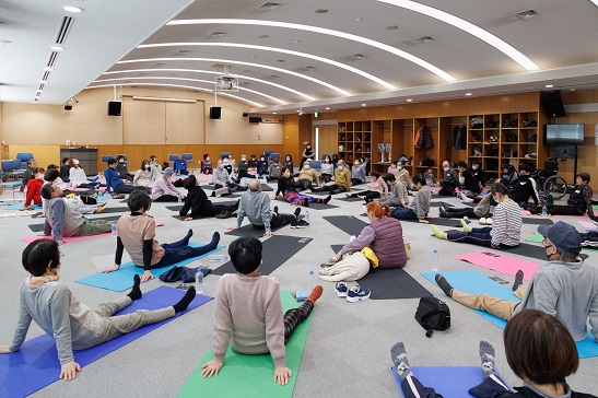 部屋の全景。ヨガマットの上で長座になった多数の参加者。大きめの部屋は隙間がないくらい参加者で埋め尽くされました。